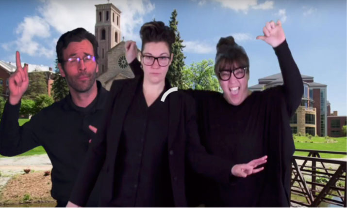 Three people dressed in black dance in front of backdrop of St. Catheirne University