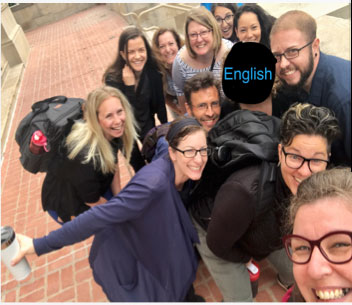 Group of people staring up at camera in group photo - one person's face is obsurbed with black overal that says English